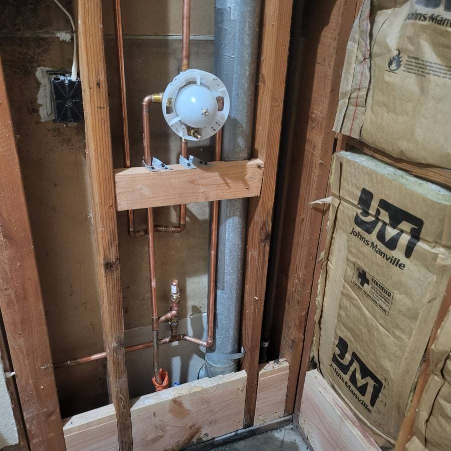 Newly installed shower valve and copper piping behind open wall framing